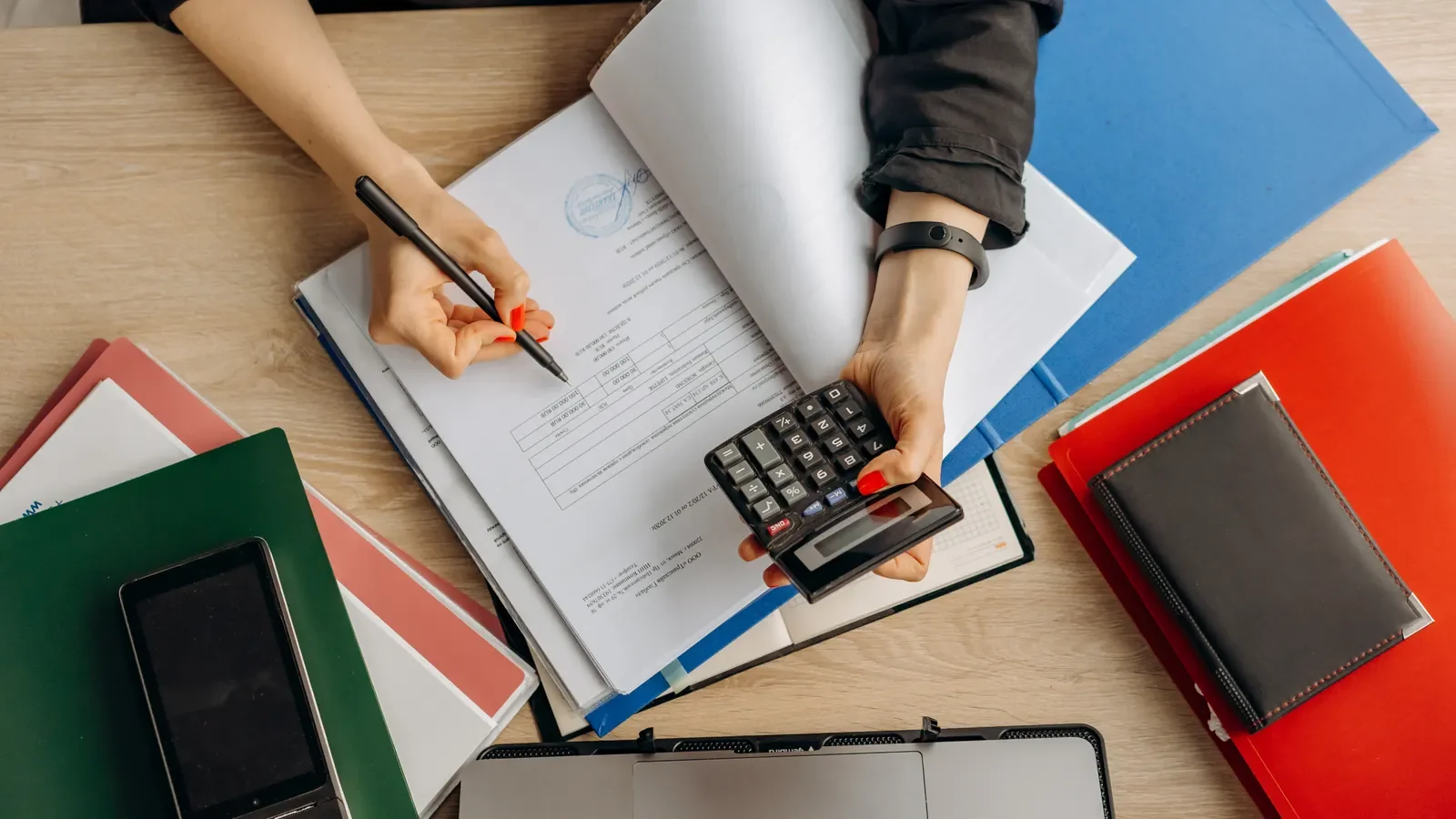 Financial documents being reviewed with a calculator, pen and laptop on a desk